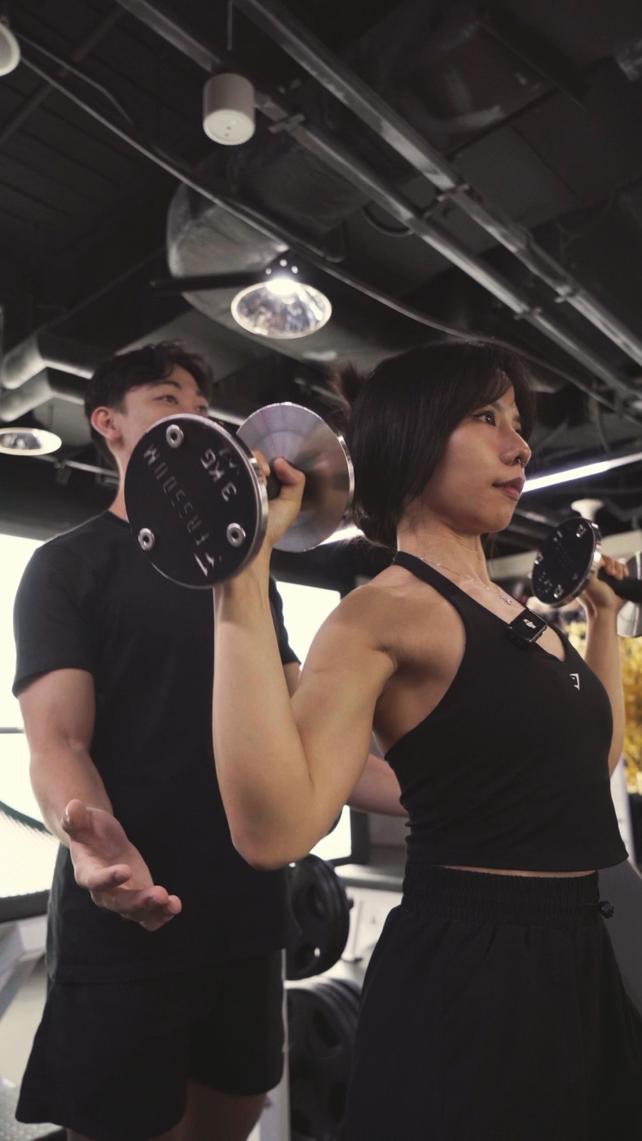 Trainer coaching a client through a dumbbell shoulder press